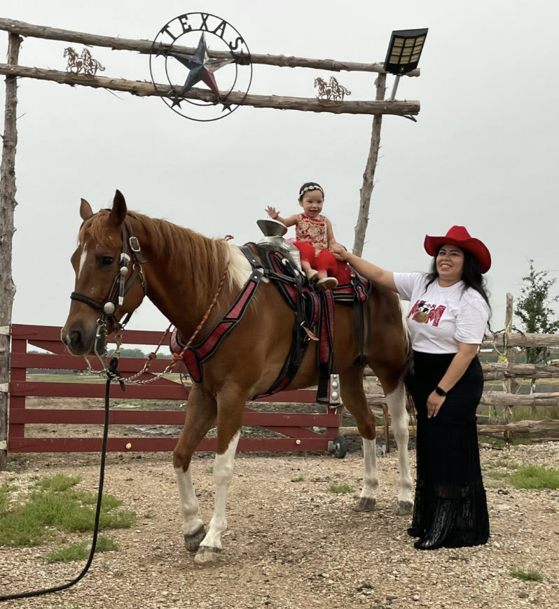Niña montada a caballo bajo el arco del rancho