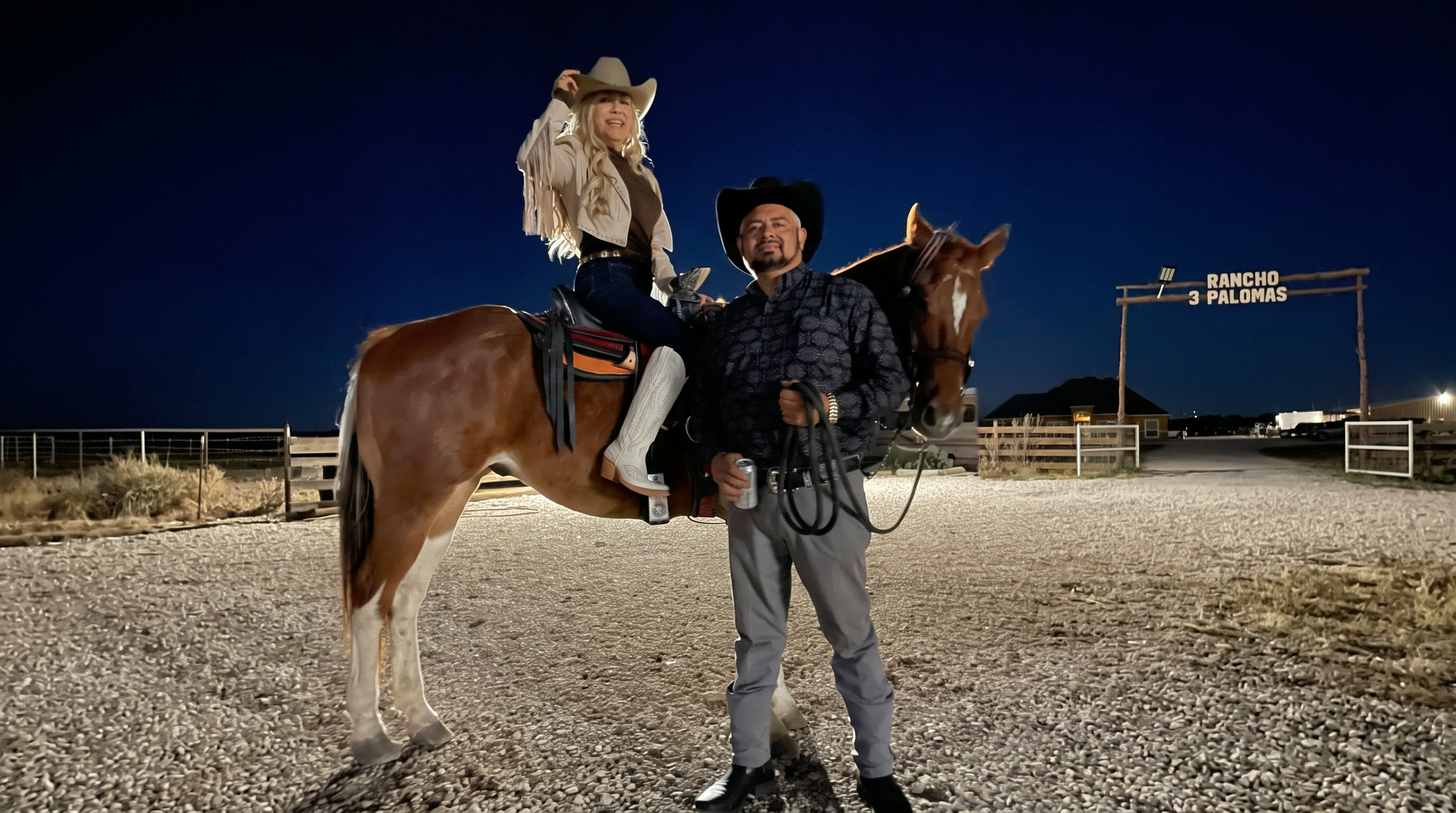 Pareja con su caballo frente al letrero iluminado del rancho de noche
