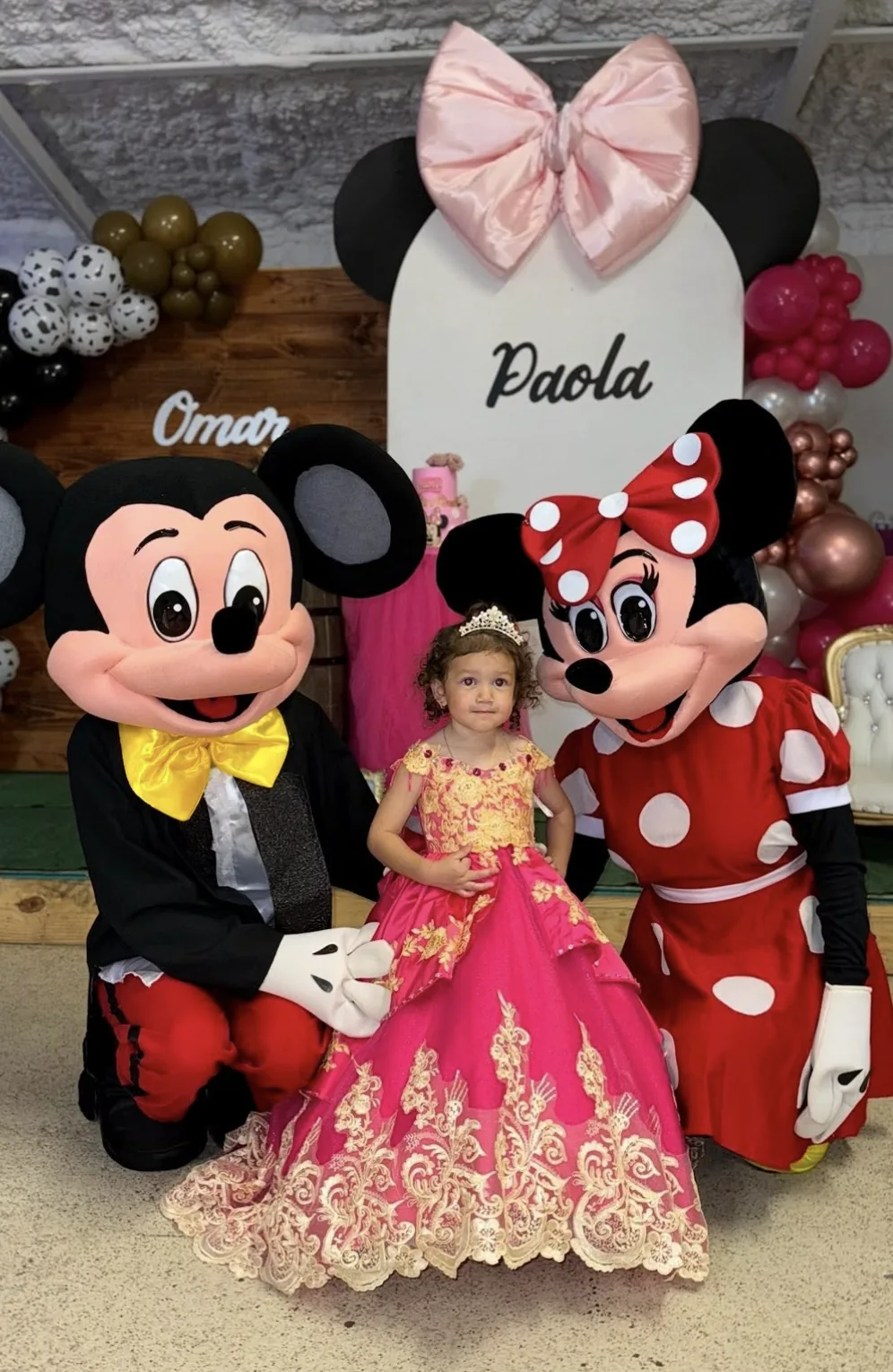 Niña con vestido rosa entre personajes de Mickey y Minnie en una celebración de cumpleaños